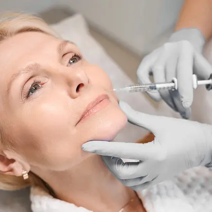 Close up of cosmetologist hands performing rejuvenating injection on mature lady cheek in beauty salon
