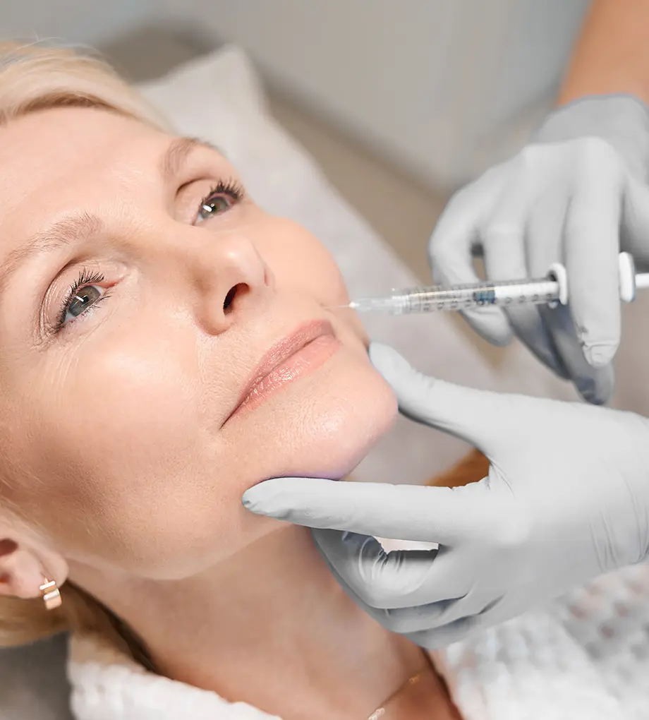 Close up of cosmetologist hands performing rejuvenating injection on mature lady cheek in beauty salon